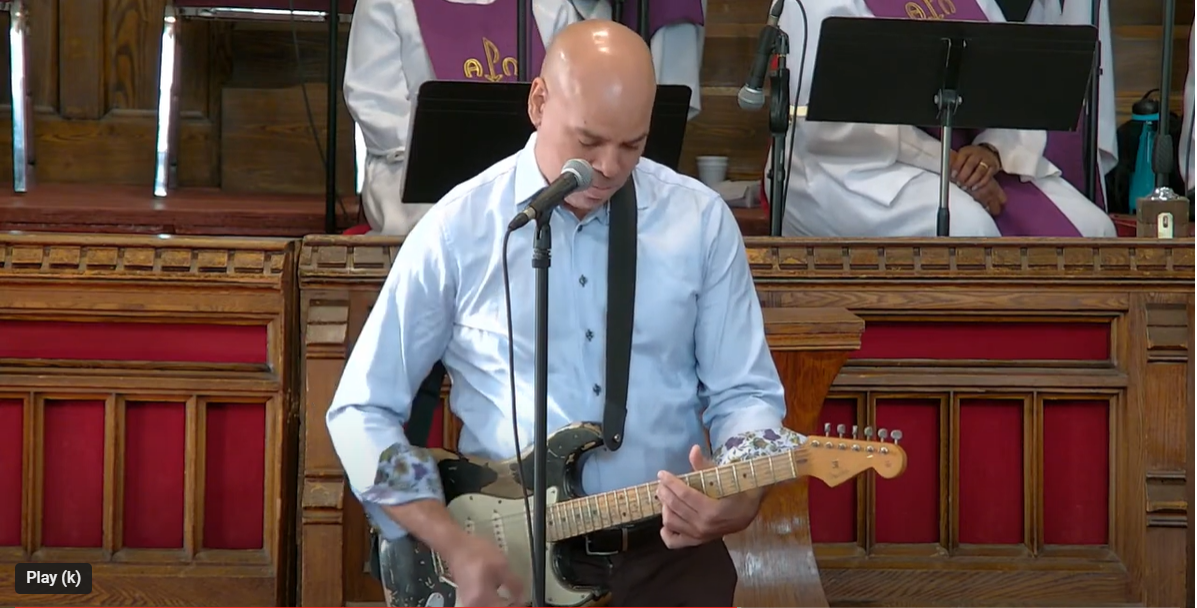 Picture of Beau Dixon holding a guitar behind a microphone in the Sanctuary of MCC Toronto