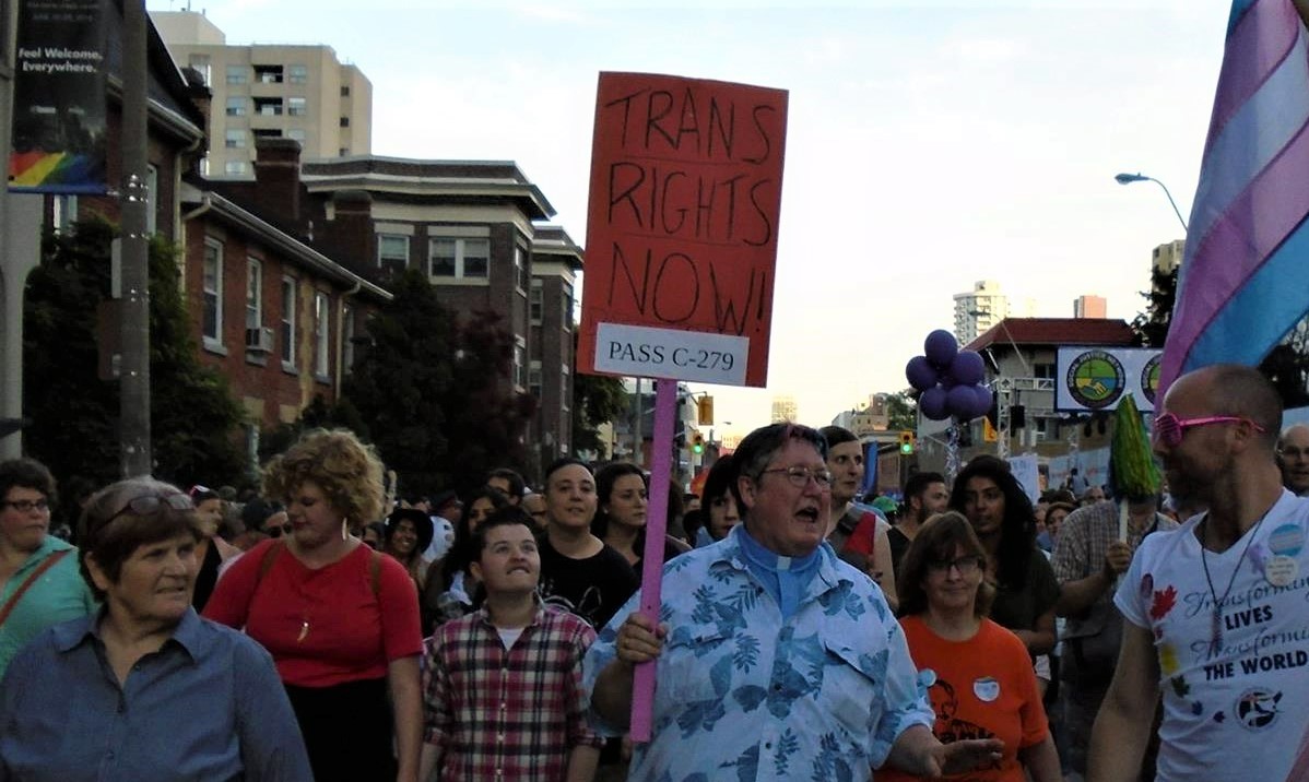 Picture of Rev. Deana Dudly at the Trans Rights rally holding a sign that says "Rights Now! Pass C-279"