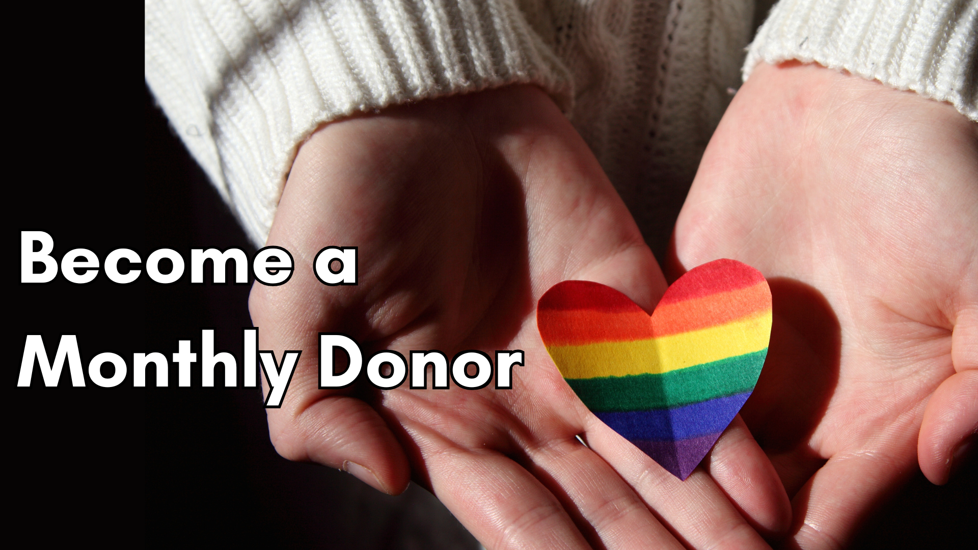 Picture of hands holding a heart-shaped pride flag with text saying Become a Monthly Donor